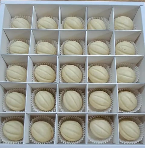 Box of 25 cream-colored confections or pastries arranged in paper cups in compartmentalized white packaging