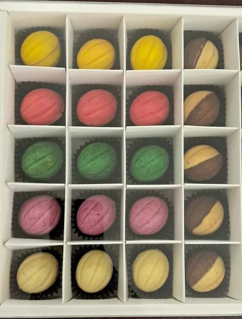 Assorted macarons in white compartmented box. Yellow, pink, green, and raspberry colored cookies with chocolate accents arranged in rows