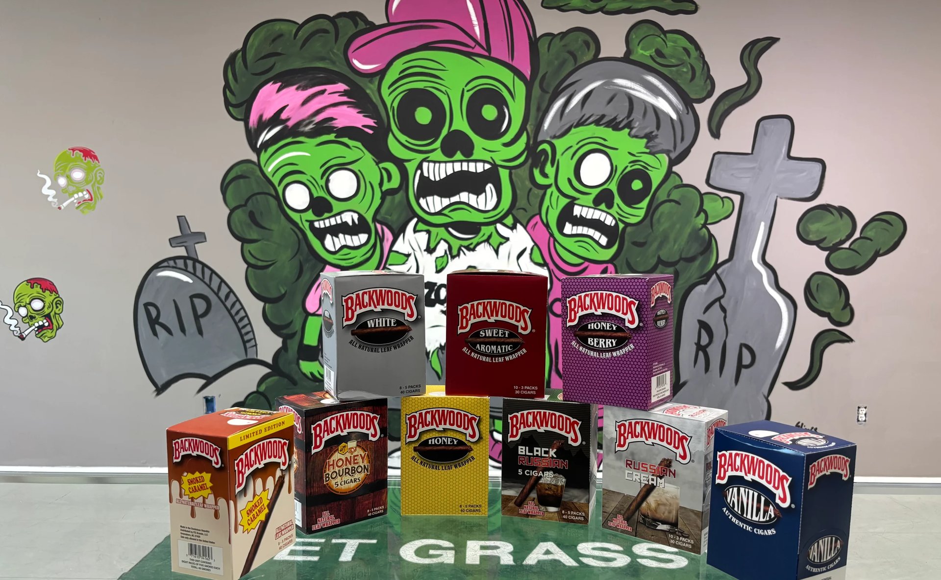 Collection of Baldwins brand beer and beverage boxes displayed with Halloween zombie face mural and tombstones