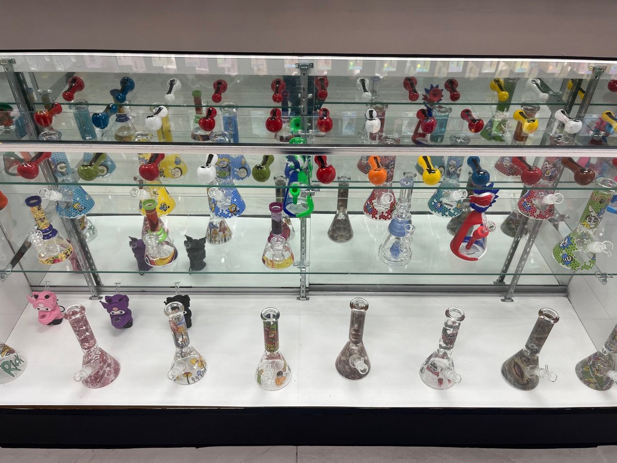 Glass display case with shelves containing colorful decorative glass pipes and smoking accessories arranged in rows