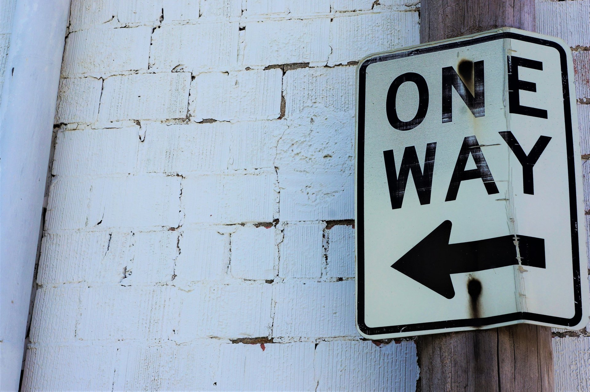 One-way street sign with left-pointing arrow mounted on white brick wall