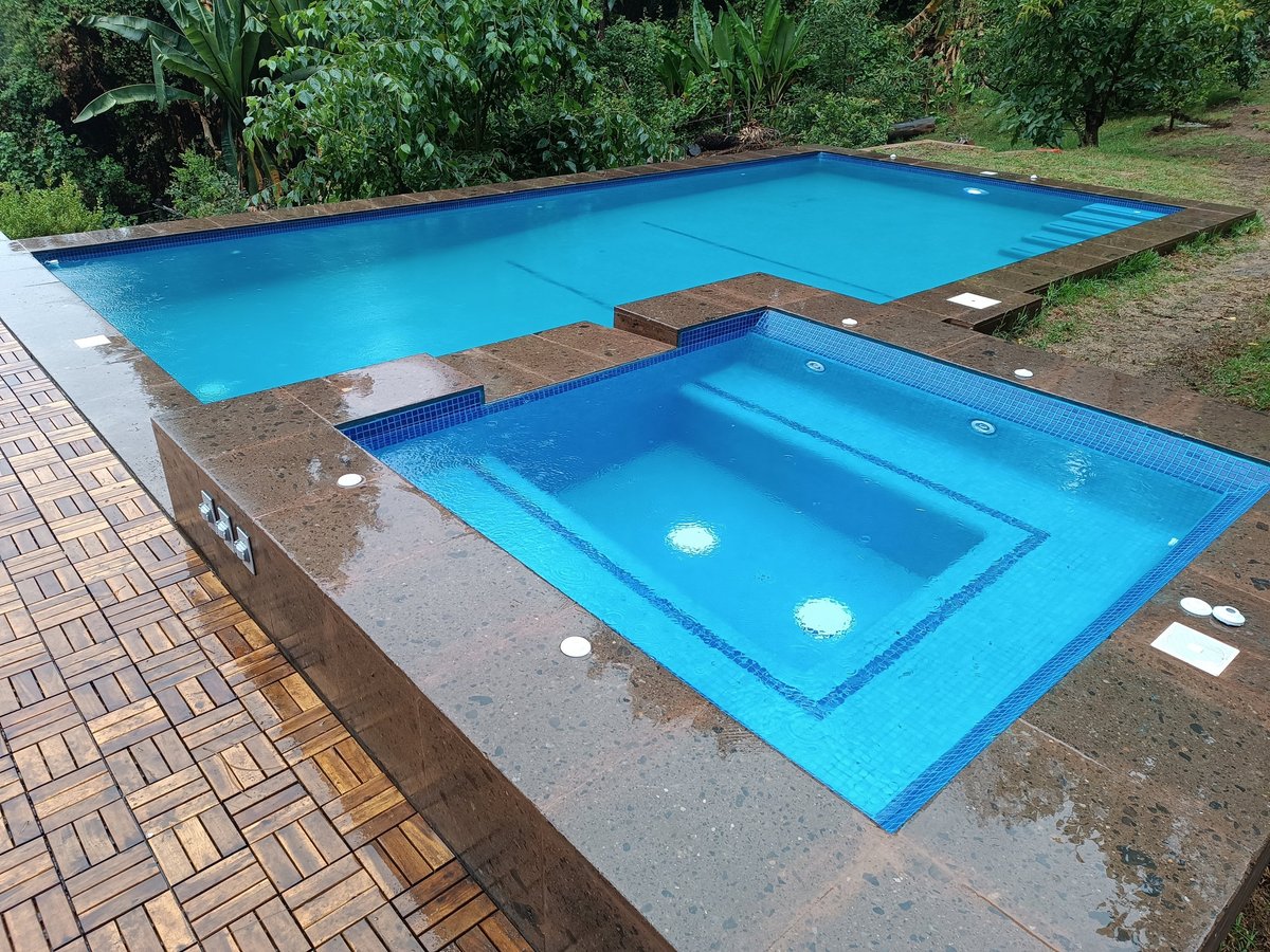 Dos albercas con agua azul brillante sobre deck pavimentado rodeado de paisaje verde y árboles