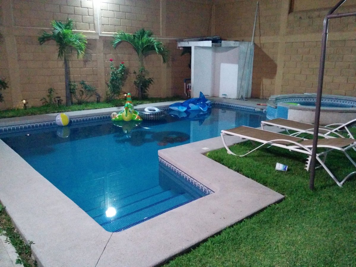 Alberca redonda con borde de azulejo amarillo y agua turquesa, rodeada de jardín y estructuras azules