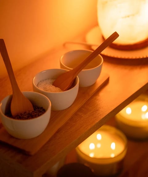 Taças com ingredientes de spa e colheres de madeira em luz quente de velas