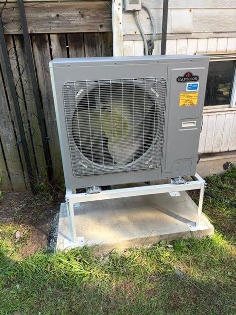 Gray Napoleon heat pump unit mounted on white metal stand against wooden building structure