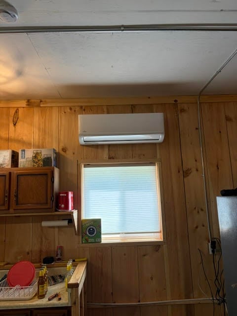Interior of wooden cabin with wall-mounted air conditioner above window, shelving, and kitchenette with various items
