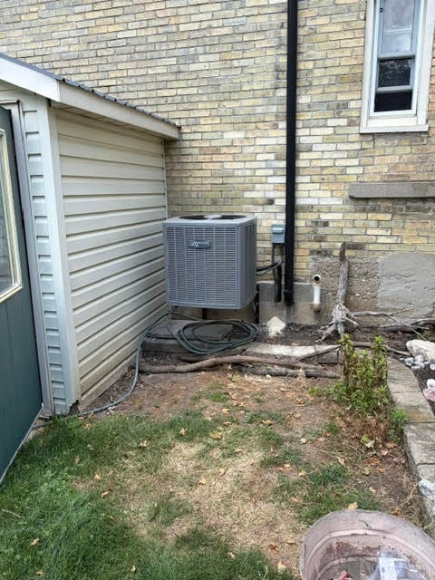 HVAC unit and coiled hose next to white garage door against brick house wall with small yard