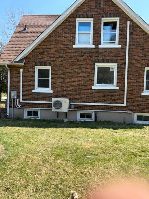 Brick house with white-trimmed windows, air conditioning unit, and green grass lawn on a clear day