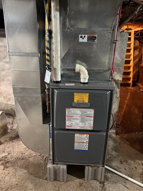 Dark metal HVAC furnace unit with warning labels and metal ducts in an indoor mechanical room