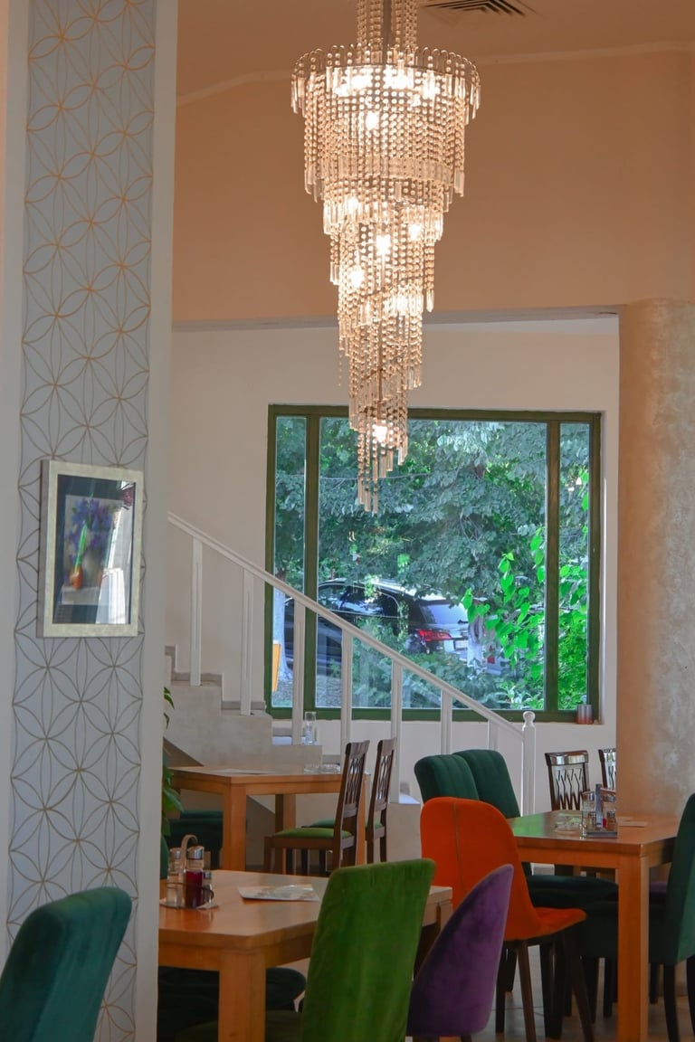 Modern dining room with multi-tiered crystal chandelier, wooden table, colorful chairs, and large windows overlooking trees