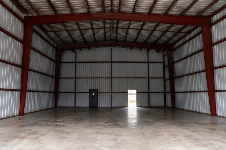 Empty warehouse interior with red metal frame, corrugated metal walls, concrete floor, and open double doors