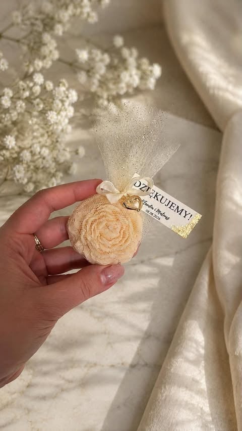 Hand holding a peach-colored fabric rose sachet with cream tulle and gold ribbon tag, surrounded by dried babys breath flowers and white fabric