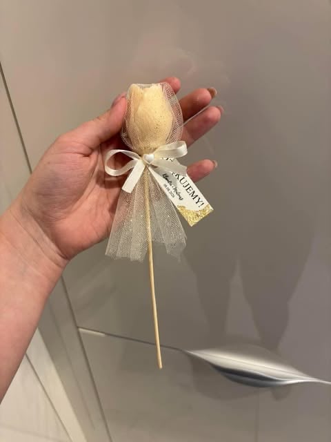 Hand holding a decorative wooden egg ornament with a cream-colored finish and cream tulle bow with tag attached