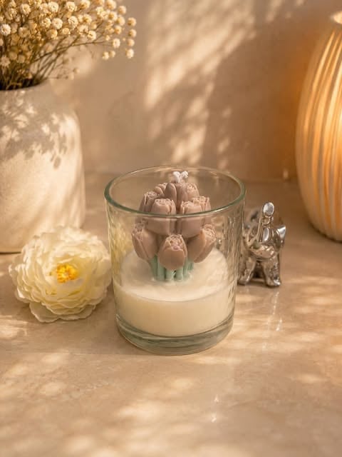 Glass candle with cream-colored wax and tulip-shaped decorative elements on a warm-toned surface with flowers and home decor