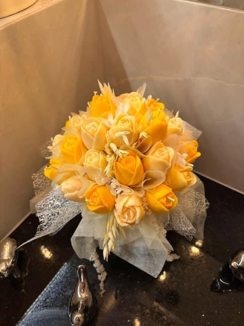 Yellow and peach roses bouquet wrapped in white tulle and ribbon, displayed on a dark surface