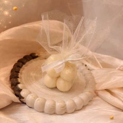Handmade wax candles arranged on decorative beaded trays with sheer tulle bow accents and gold sparkle backdrop