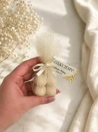 Hand holding a small mesh pouch with cream-colored product and Zielujemy label against white textured background