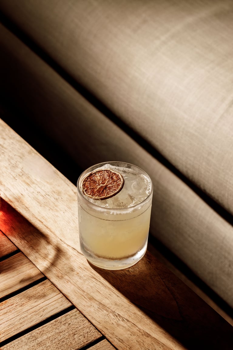 Clear cocktail with ice and dried citrus slice garnish on wooden surface near neutral fabric background