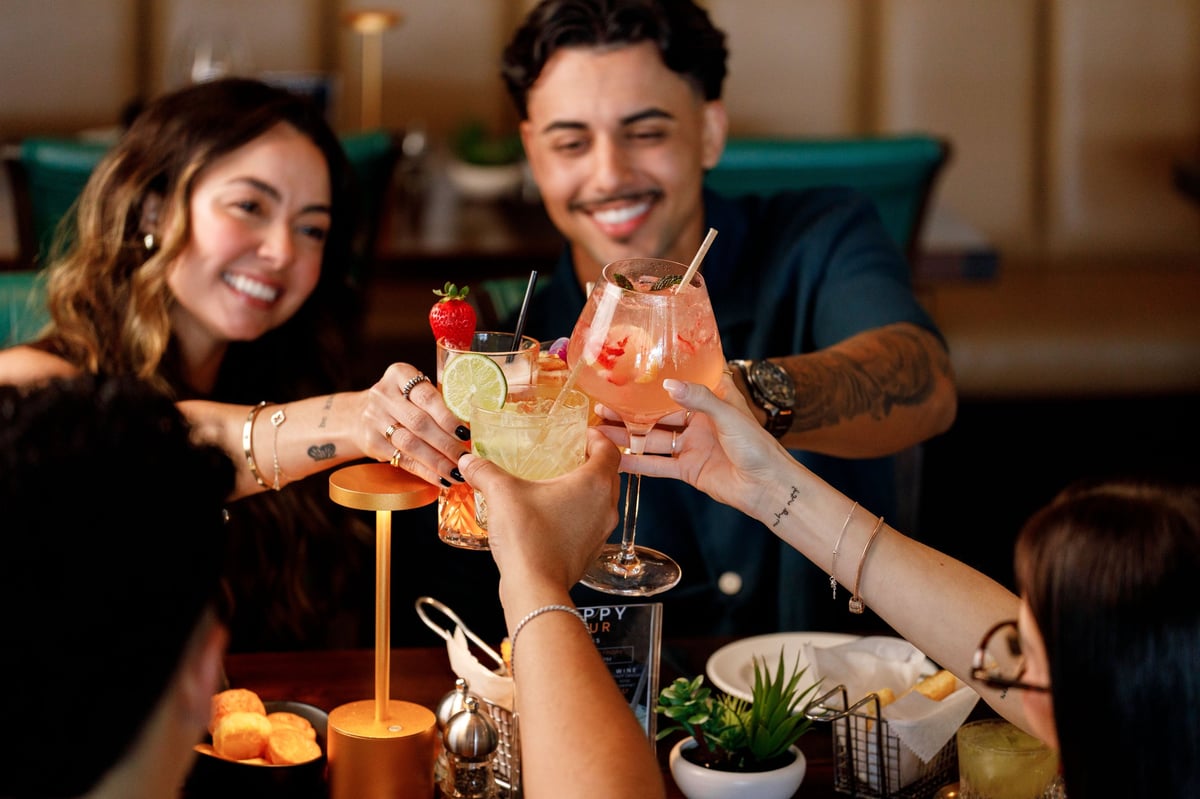 Group of friends toasting with cocktails at an indoor gathering, clinking glasses together in celebration