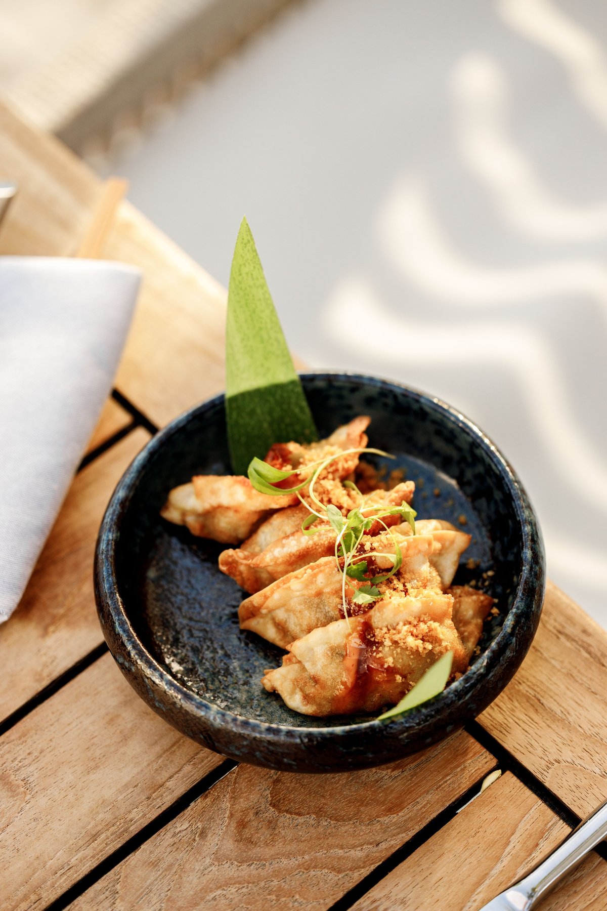 Fried dumplings in a black bowl on a wooden table with green leaf garnish and chili oil