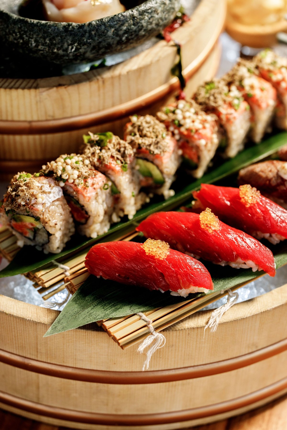 Assorted nigiri sushi arranged on bamboo with steamed dumplings in basket above