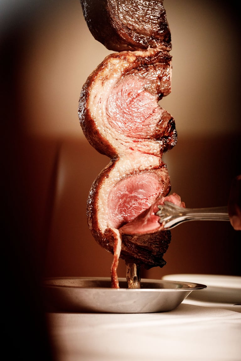 Sliced roasted meat stacked on a fork, showing pink interior with caramelized brown crust, against warm lighting