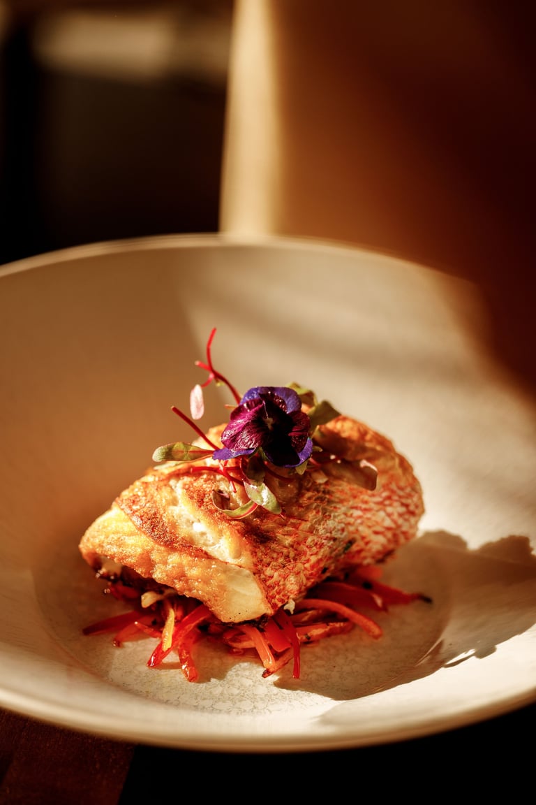 Gourmet plated dish with golden-seared fish, red beet strands, and a purple edible flower on white ceramic plate