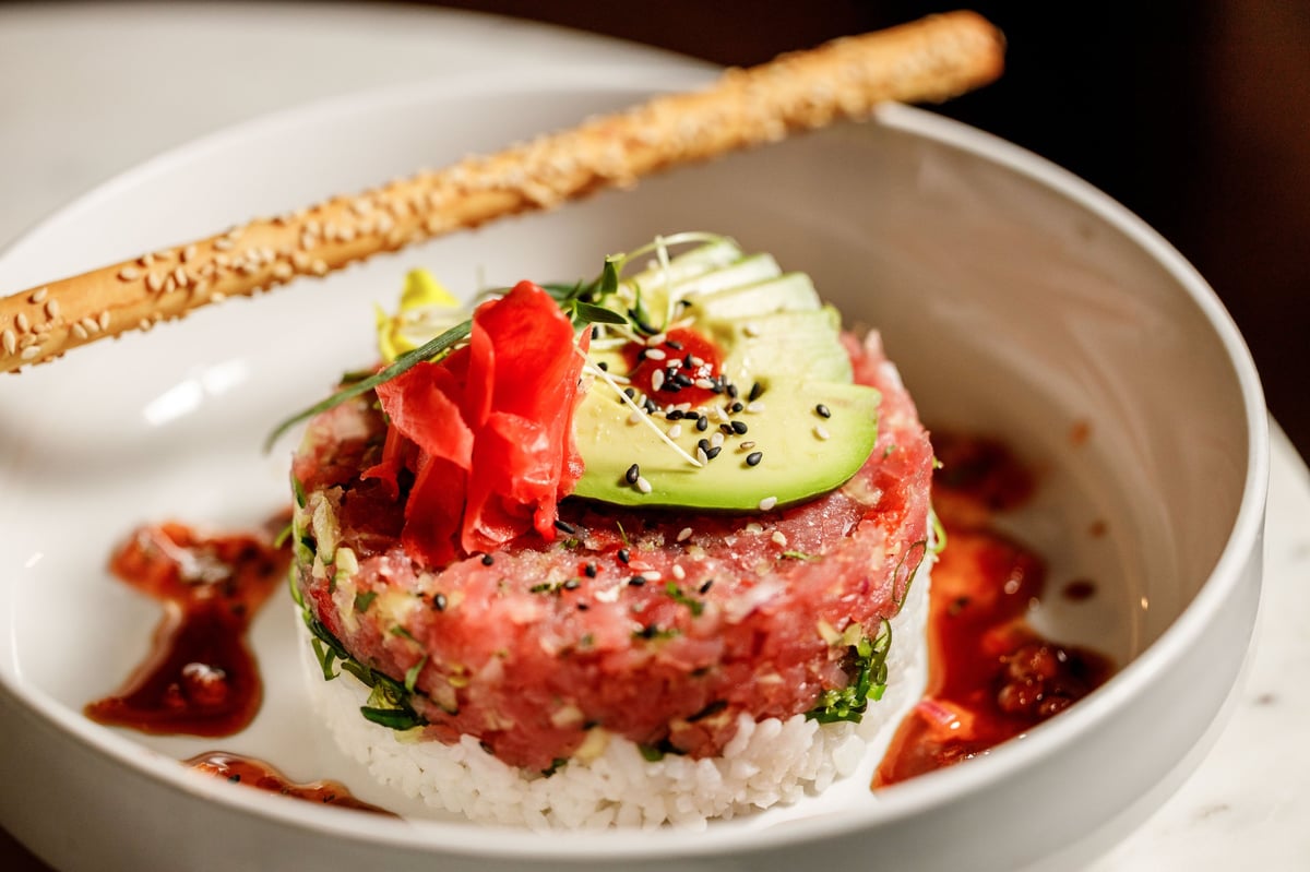 Plated tuna tartare appetizer with avocado, ginger, red dots, sesame breadstick, on white plate