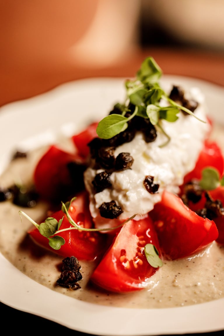 Plated dessert with tomato wedges, whipped cream, black caviar, and microgreens on a beige base