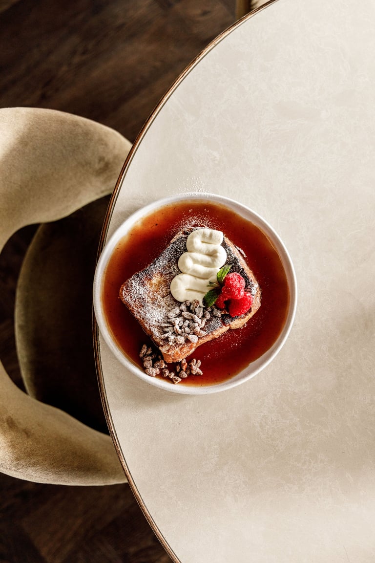 Elegantly plated dessert with chocolate cake, red berry sauce, whipped cream, and fresh strawberry garnish on a white plate