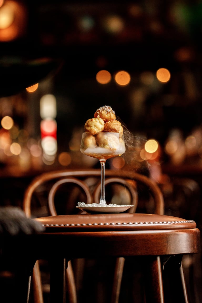 Gourmet dessert in a wine glass with caramel sauce on a wooden table in an upscale restaurant with warm bokeh lighting