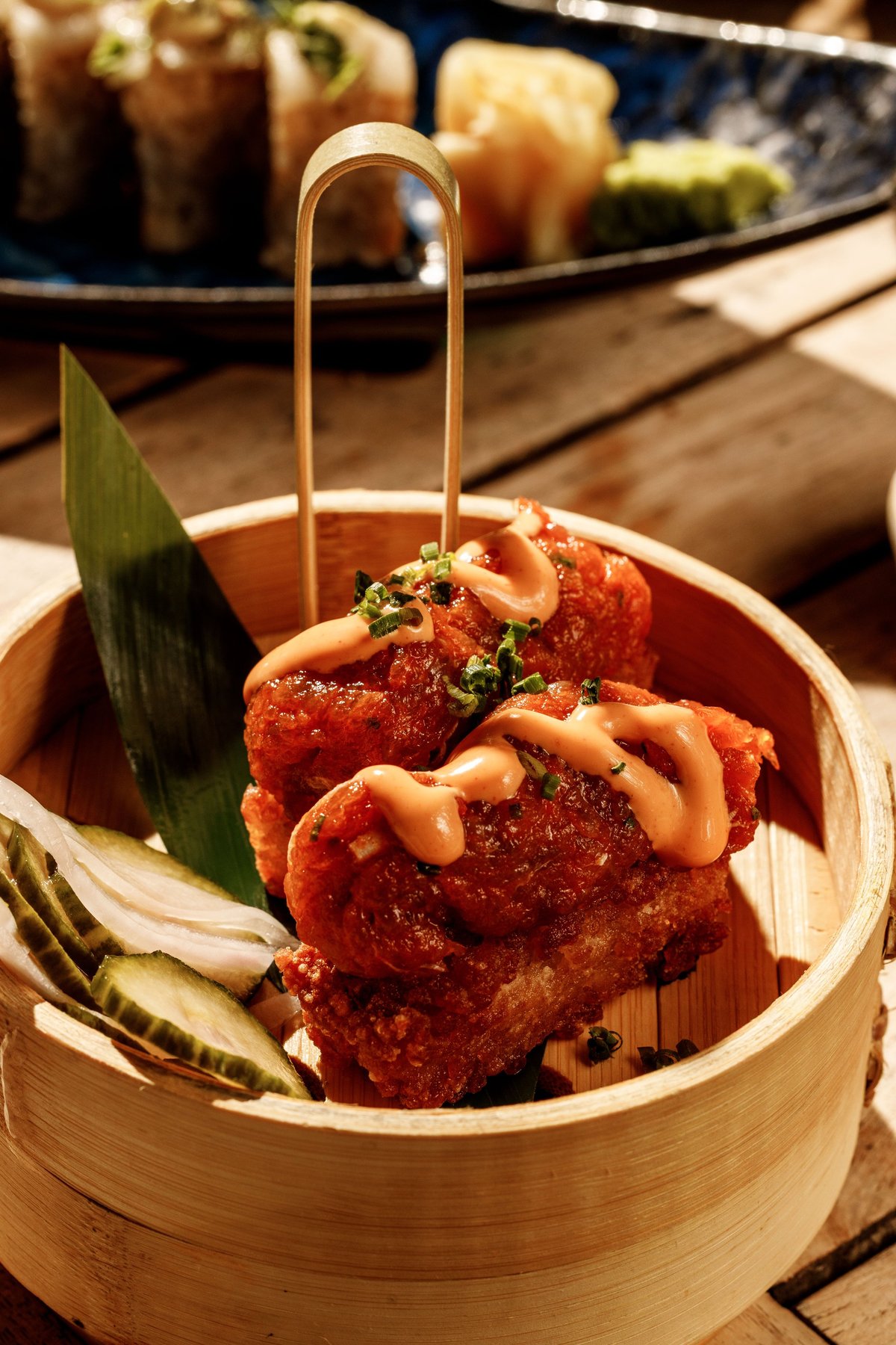 Crispy red fried dumplings with creamy sauce and microgreens in a bamboo steamer basket