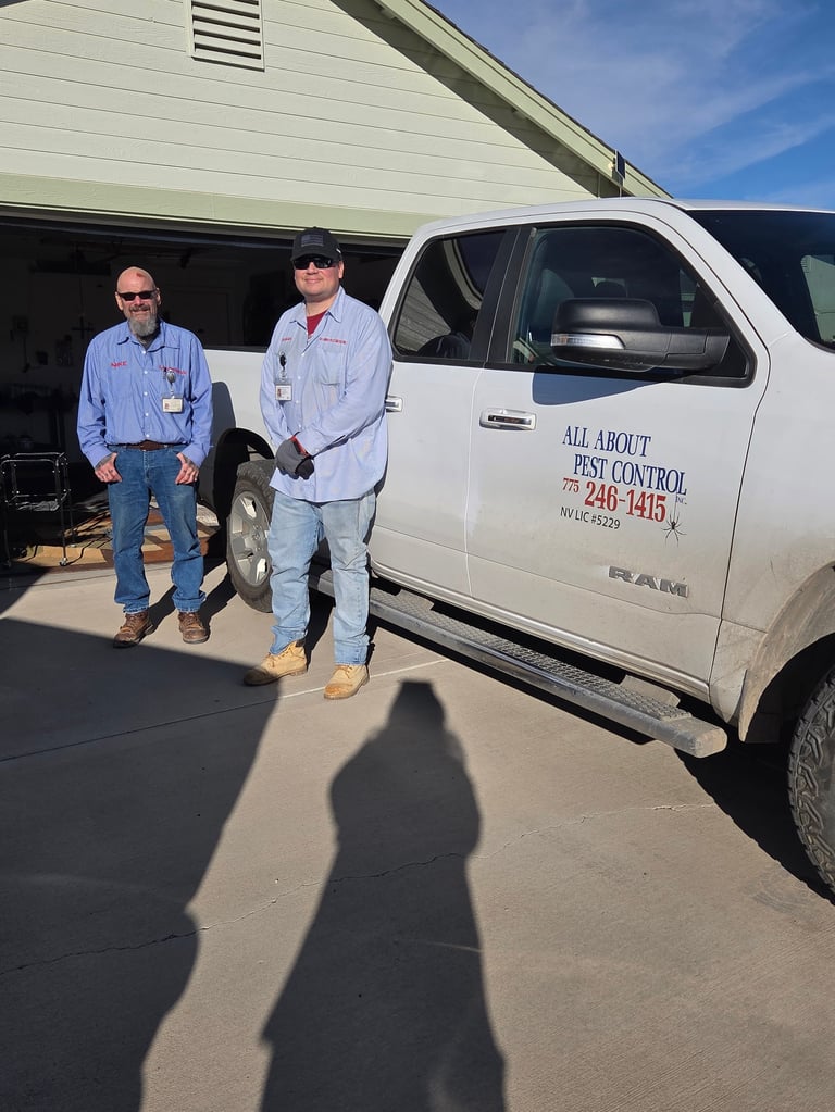 Two men in work uniforms standing beside a white pest control service truck in a driveway