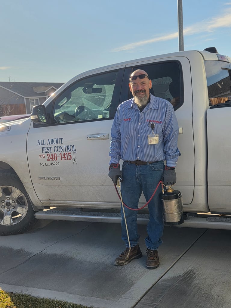 Pest control worker standing in front of a white service van holding equipment, wearing blue work shirt and sunglasses