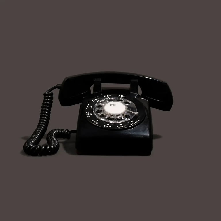 Black vintage rotary telephone with coiled cord handset against gray background