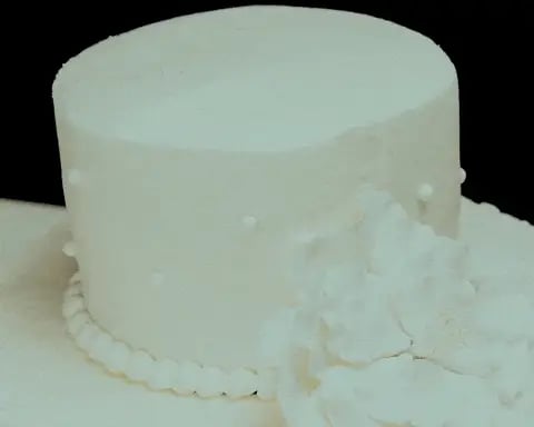 White frosted wedding cake with cylindrical shape and scalloped base on black background