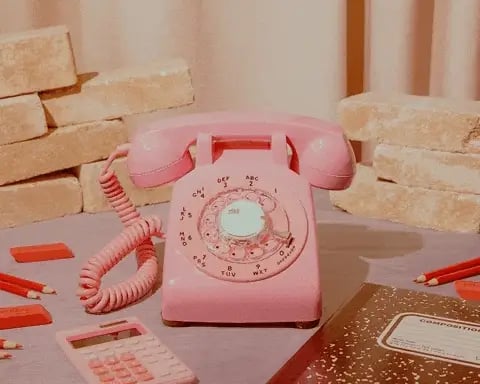 Vintage pink rotary telephone on a desk with office supplies and brick wall backdrop