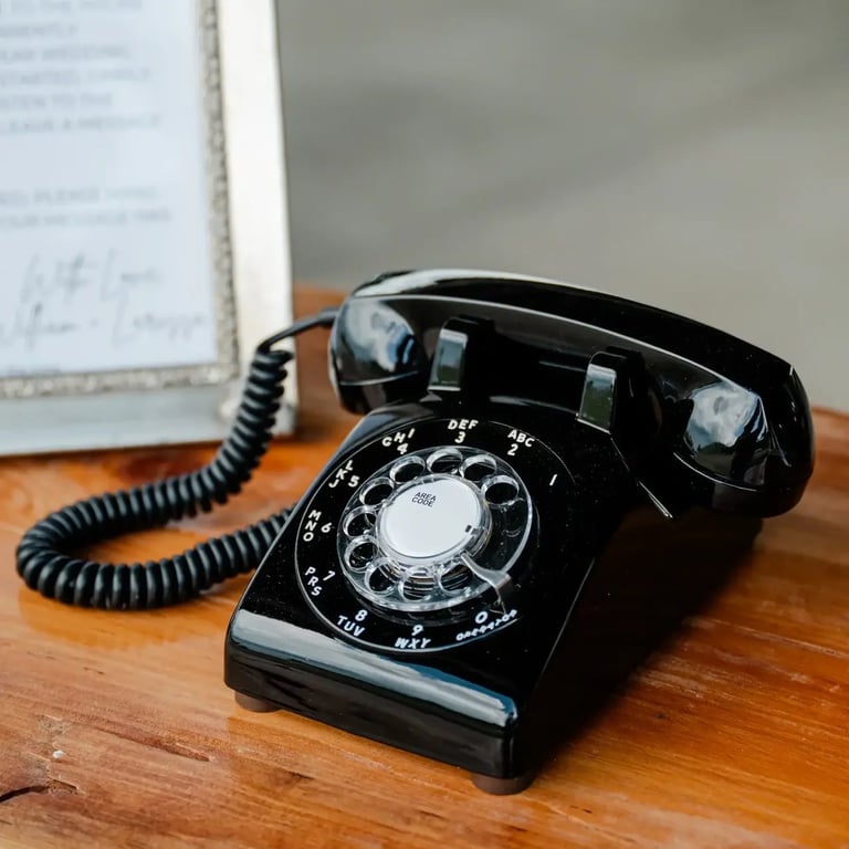 Black rotary telephone with coiled cord on wooden desk next to a document
