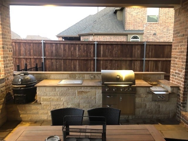 Backyard outdoor kitchen with brick patio, stone counters, built-in grill and smoker, wooden privacy fence