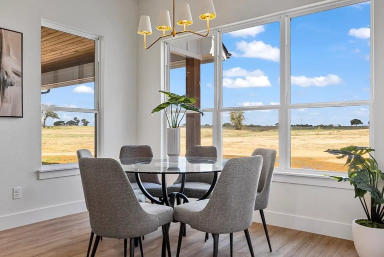 Modern dining room with gray upholstered chairs around a round black table, gold light fixture, large windows
