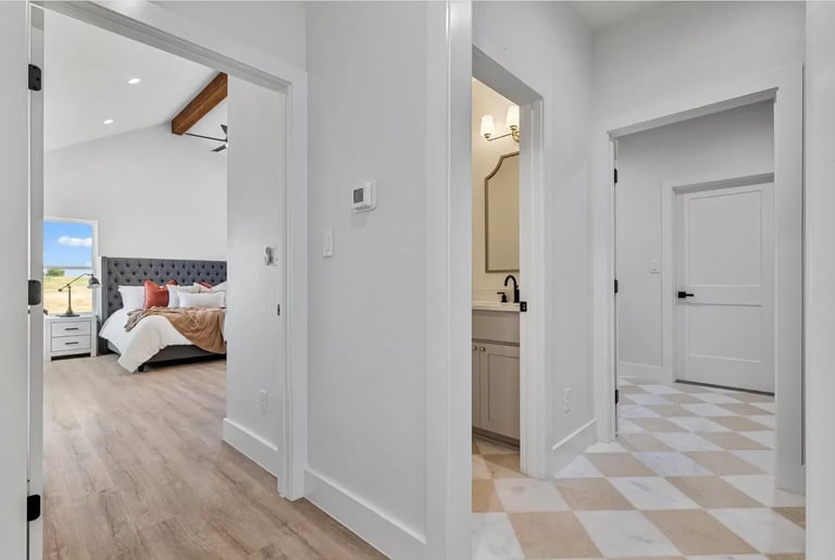 Modern hallway with white walls leading to a bedroom with wood flooring and a bathroom doorway on the right