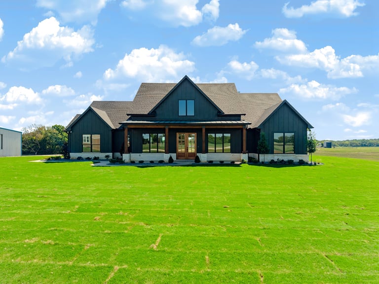 Front elevation of the modern farmhouse custom home in Whitesboro, Texas — dark siding, timber entry and large front lawn