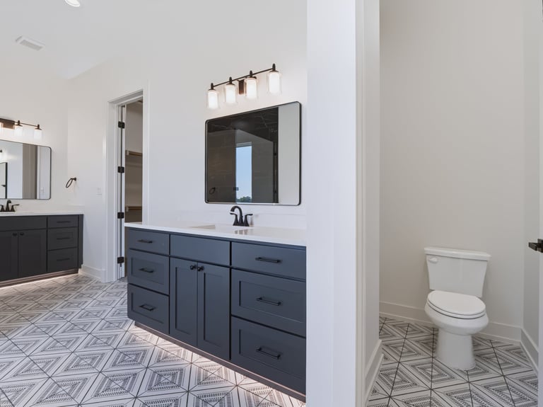 Modern bathroom with dark blue vanity, mirror, and black light fixture, with geometric floor tile and separate toilet area