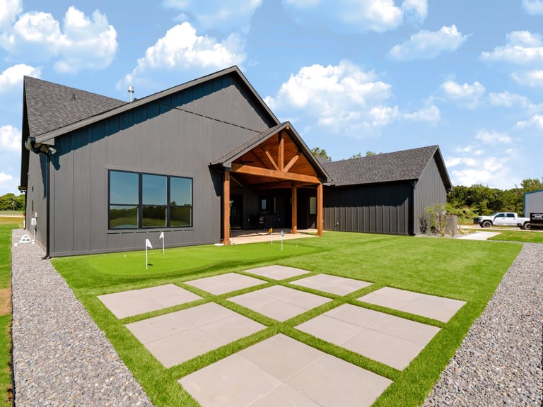 Modern farmhouse exterior with gray siding, wooden entrance awning, and geometric concrete pathway through green lawn