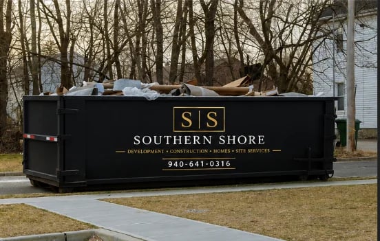 Black dumpster with Southern Shore branding and contact number on a residential driveway near bare trees
