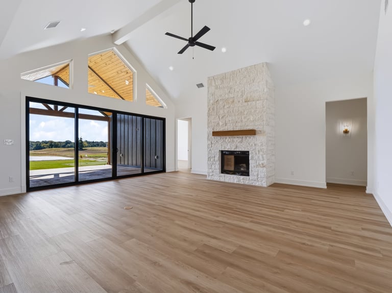 Modern living room with hardwood floors, stone fireplace, large glass doors, and vaulted ceiling with skylights overlooking a golf course.