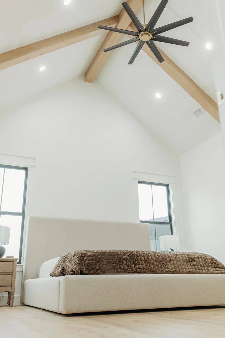 Modern bedroom with cream upholstered bed, exposed wood beams, and recessed lighting in vaulted ceiling