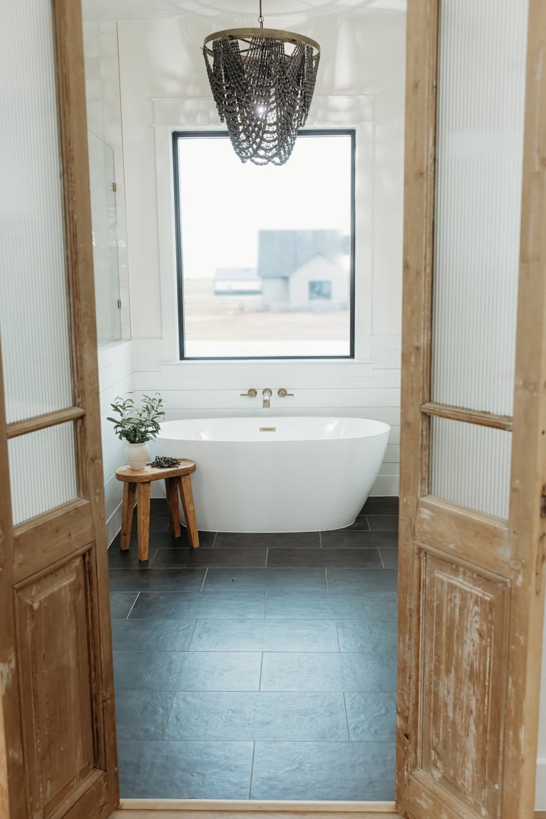 Bathroom in the completed Whitesboro custom home — freestanding white bathtub on slate tile flooring with a pendant light, reclaimed wood doors and a large window