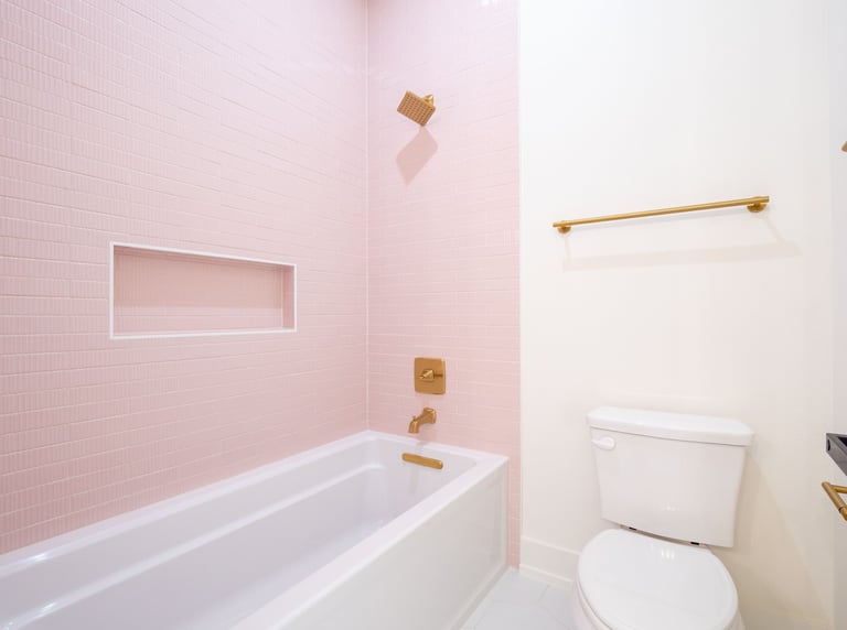 Modern bathroom with pink tile walls, white bathtub, toilet, brass fixtures, and built-in shelf alcove