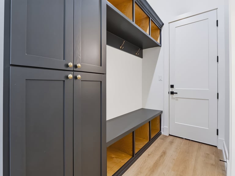 Modern entryway with dark gray cabinetry, wooden shelving, gray countertop, and white door on light wood flooring